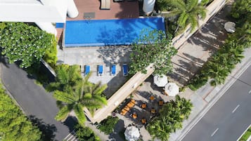 Vue aérienne d’un hôtel doté d’une piscine, d’un espace extérieur aménagé avec des sièges et de palmiers.