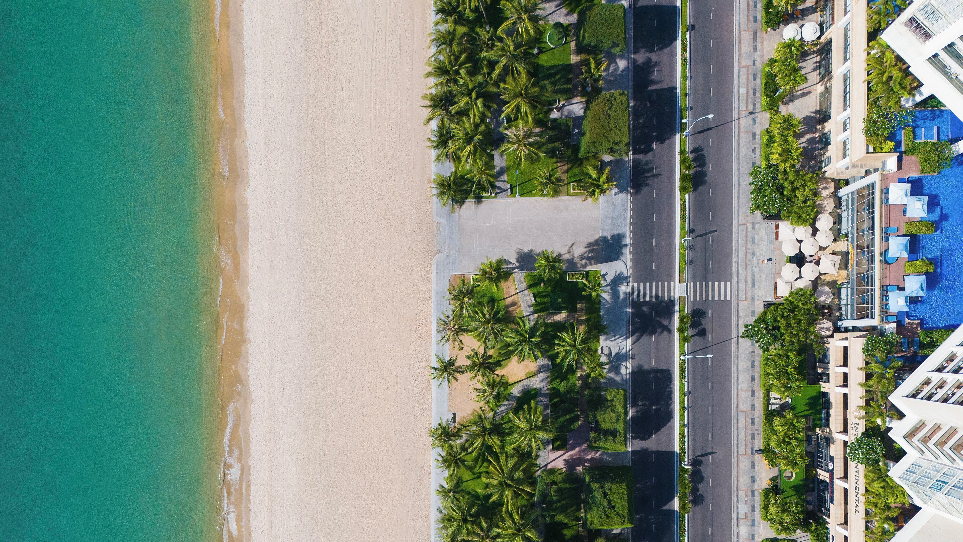 Vista aerea di un hotel sulla spiaggia, con una strada, palme e una piscina.