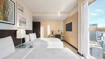 A hotel room with two beds, a desk, a TV, and a large window with a city view.