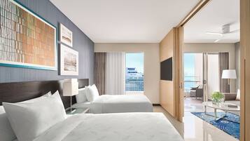 A hotel room with two beds, a large window with a city view, a balcony with seating, and a flat-screen TV.