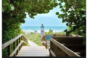 A wooden pathway leading to a beach with a signboard and a railing.