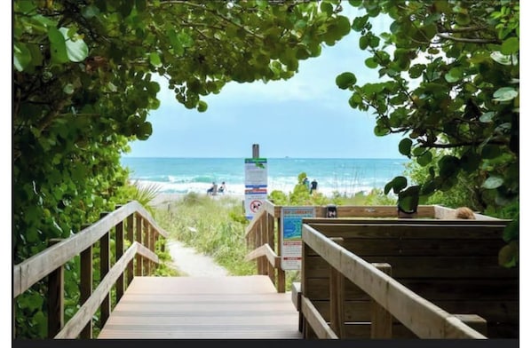 Ein Holzweg führt zu einem Strand, mit einem Schild und einer Geländer.