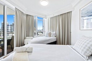 A hotel room with two beds, a balcony, and a city view.