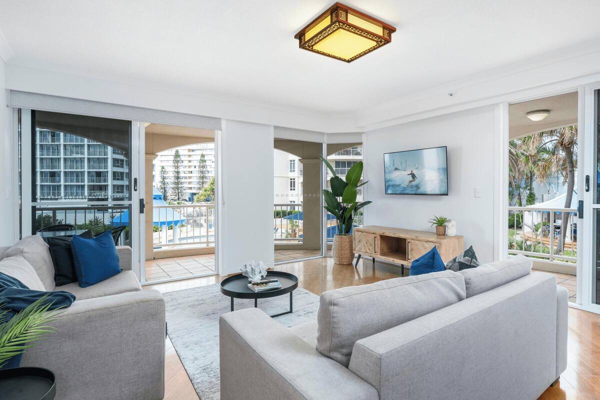 Amplia sala de estar con un sofá gris, una mesa de centro y un ventanal con vistas a un balcón y zona exterior.