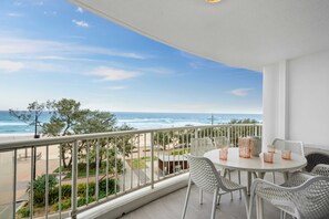 A balcony with a view of the beach and ocean, white wicker furniture, and a white table.