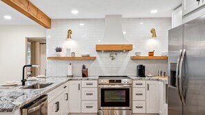 Una cocina moderna con armarios blancos, un refrigerador de acero inoxidable, horno empotrado y encimera de mármol.