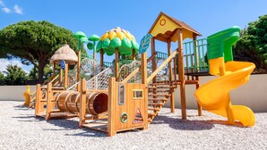 A playground with a slide, climbing structures, and a thatched-roof playhouse. - Mobil-home VIP | Clim & Plancha | Plage à 700 m (Vendres)