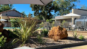 An outdoor seating area with tables and umbrellas, surrounded by plants and a large rock.