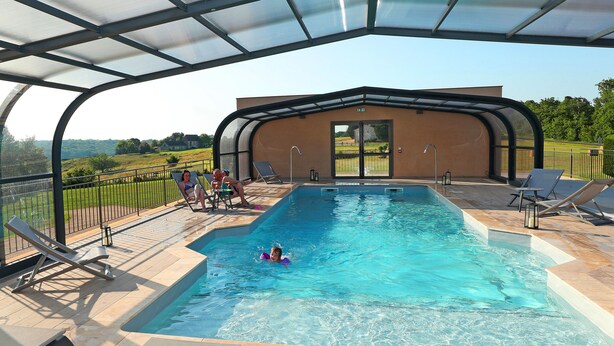An indoor swimming pool with clear blue water, surrounded by lounge chairs and a covered patio area.