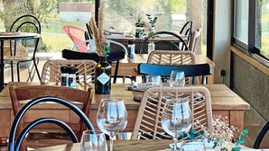 A dining area with wooden tables and chairs, a bottle of Rocero wine, and a view of the outdoors.