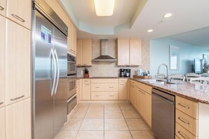 A modern kitchen with stainless steel appliances, light wood cabinetry, and a granite countertop. - Stunning Three Bedroom Bayside Condo with Complimentary Boat Slip. (Orange Beach)