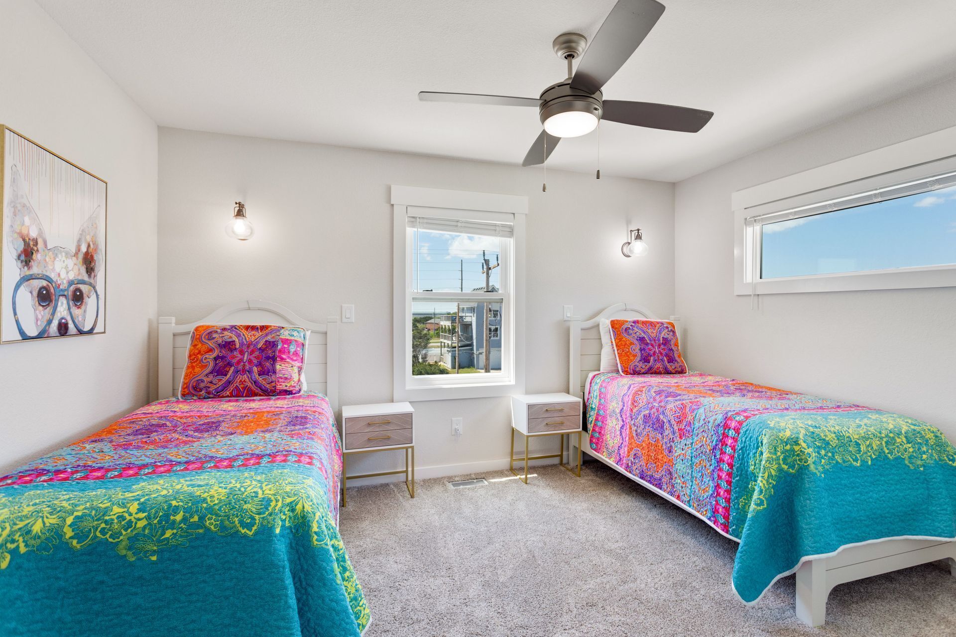 A bedroom with two beds, a ceiling fan, a window, and artwork on the wall.