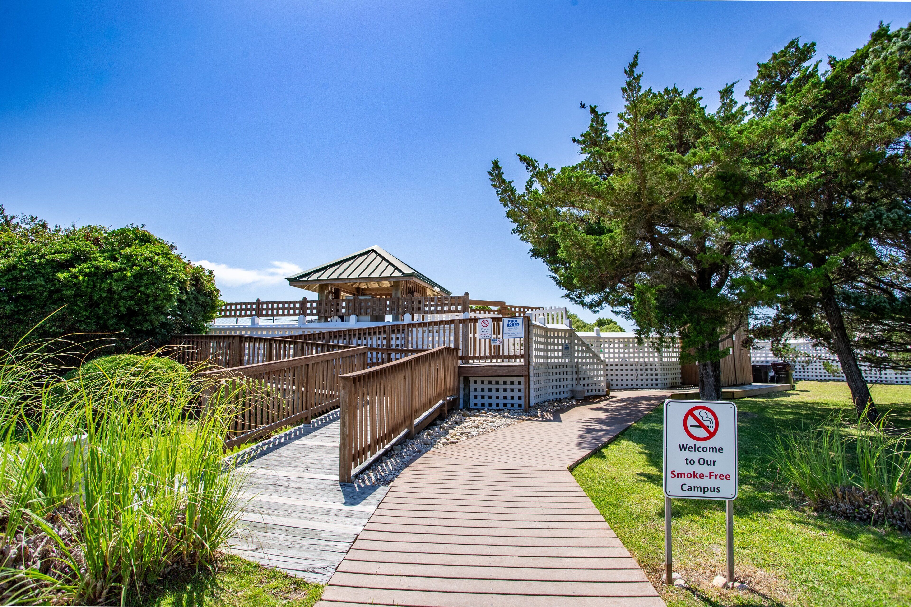 A smoke-free campus entrance with a wooden pathway, a covered pavilion, and a sign welcoming visitors.