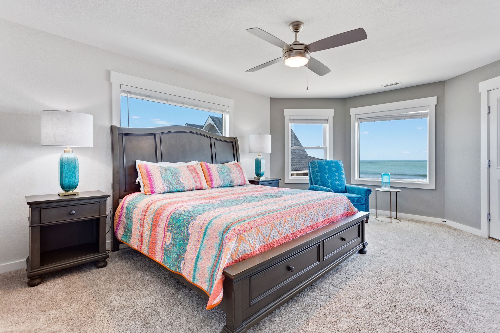 A bedroom with a bed, two nightstands, a ceiling fan, and a view of the ocean.