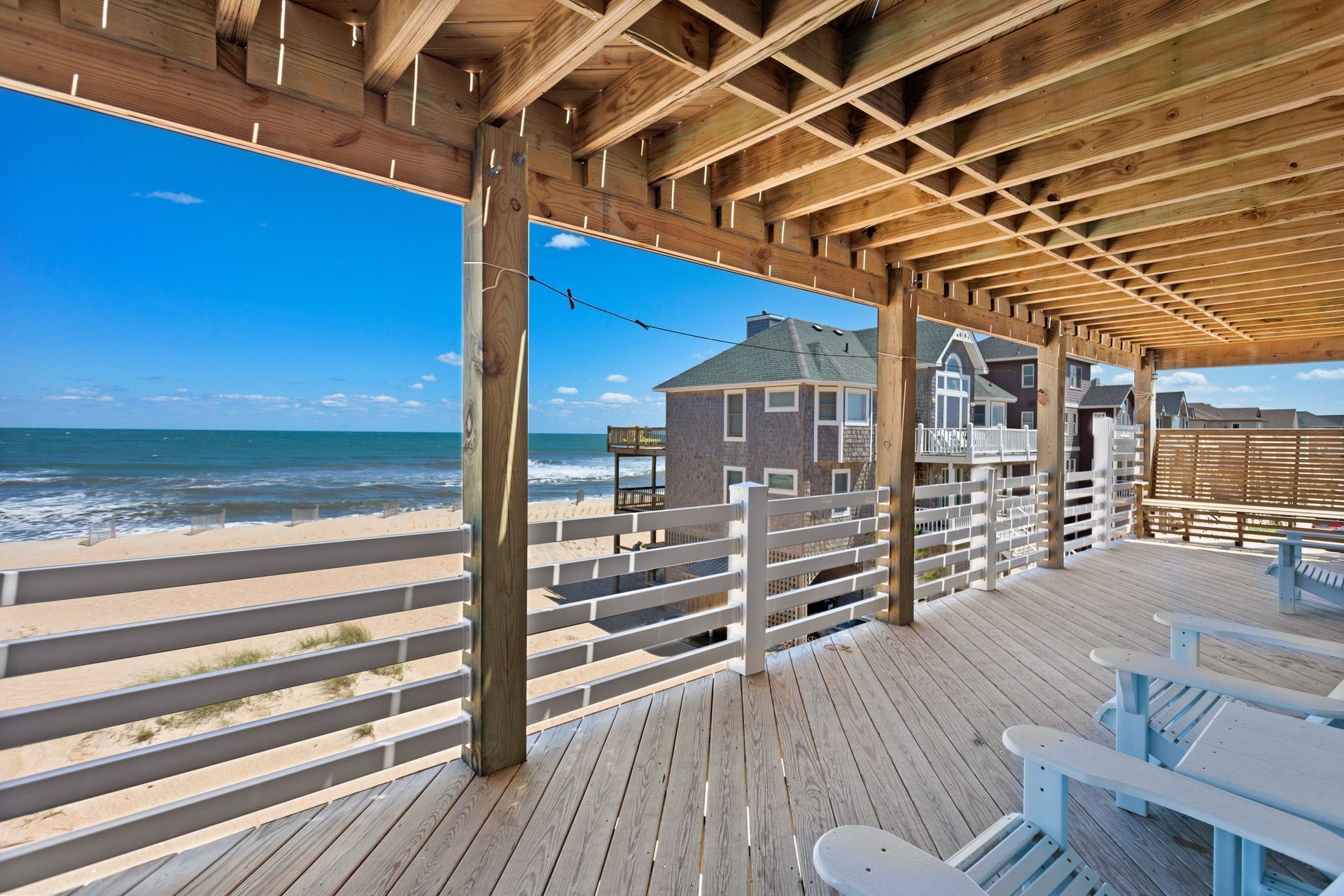 A wooden deck with a view of the beach and ocean, featuring a house with a balcony and a fence.