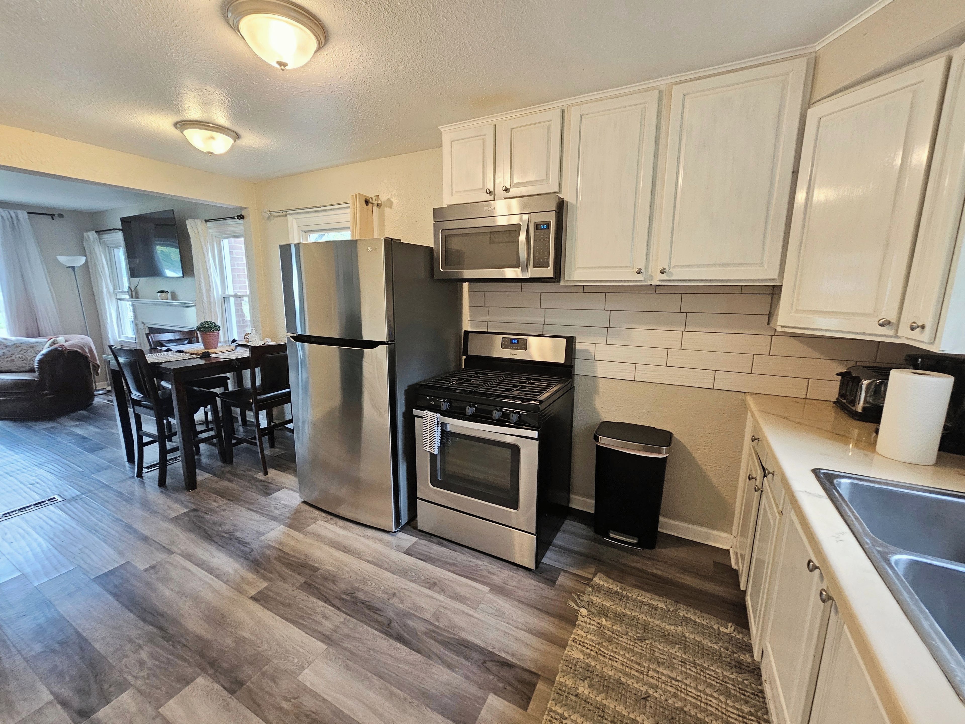 A modern kitchen with stainless steel appliances, white cabinetry, and a dining area with a table and chairs.