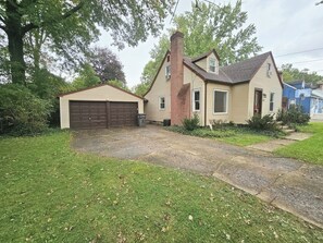 A two-story house with a garage, a chimney, and a front yard with grass and shrubs. - 4 bd Pet-Friendly Home- Steps to Millcreek Park (Youngstown)