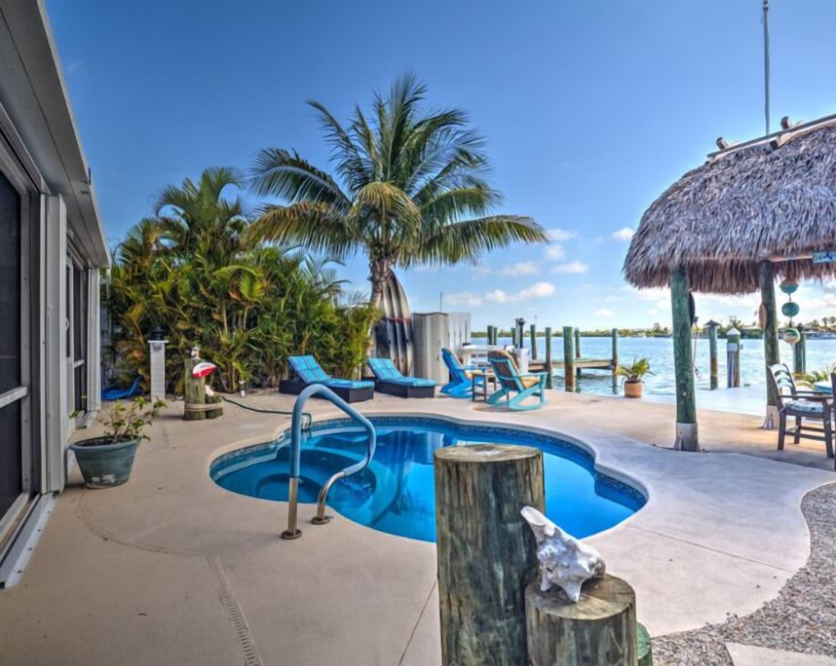 A pool area with lounge chairs, a thatched-roof structure, and palm trees.