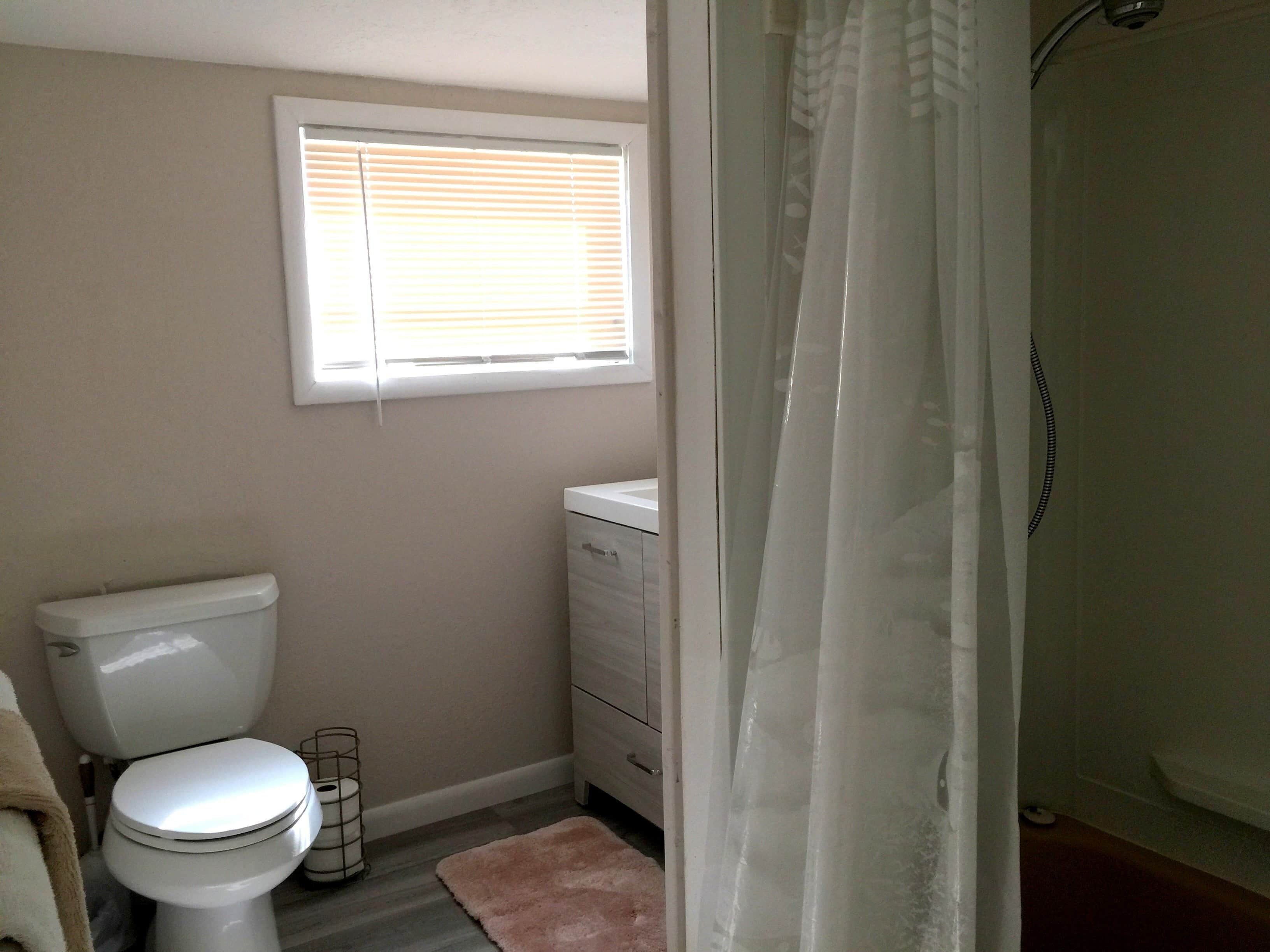 Une salle de bain avec des toilettes, un petit meuble, une fenêtre et un rideau de douche.