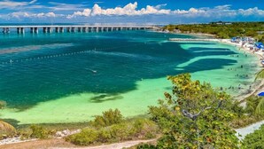 A coastal view with clear turquoise waters, a pier, and a beach with people. - Capt. Joe's Key Colony Beach 5-Star Pool & Beach access (Key Colony Beach)