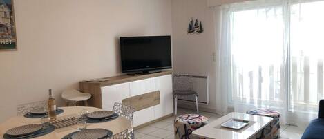 Una sala de estar moderna con comedor, televisor y un amplio ventanal.