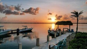A sunset view with boats docked at a pier, a thatched-roof structure, and a palm tree. - Venture Out Million Dollar Ocean View (Cudjoe Key)