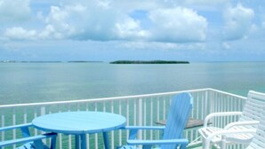 A deck with a round table and two chairs, overlooking a calm sea with a small island in the distance. - Venture Out Million Dollar Ocean View (Cudjoe Key)