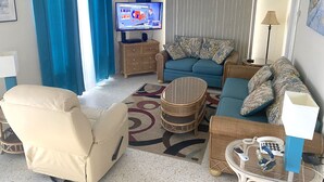Ein Wohnzimmer mit Fernseher, einer Couch, Sesseln und einem gemusterten Teppich.