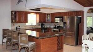 Una cocina moderna con armarios de madera, una isla grande, electrodomésticos de acero inoxidable y sillas de mimbre.