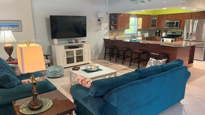 Un salón moderno con televisor grande, asientos cómodos y una zona de cocina con taburetes de bar.