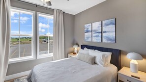 A hotel room with a large bed, two bedside tables, a nightstand, a window with curtains, and a view of a parking lot.