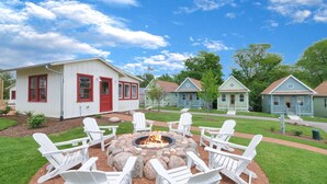 Une rangée de charmantes maisons de plain-pied, avec un foyer central entouré de chaises Adirondack blanches.
