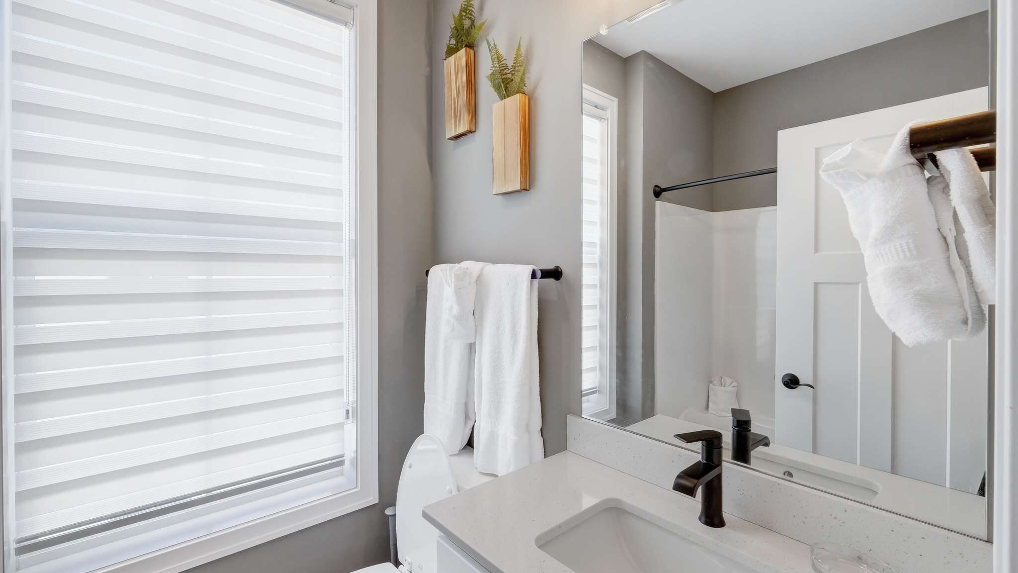 Une salle de bain moderne avec une grande fenêtre, un lavabo, un miroir et deux serviettes suspendues à un porte-serviettes.