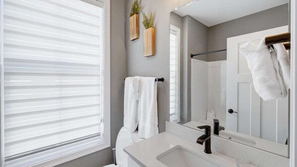 A modern bathroom with a large window, a sink, a mirror, and two towels hanging on a towel rack.