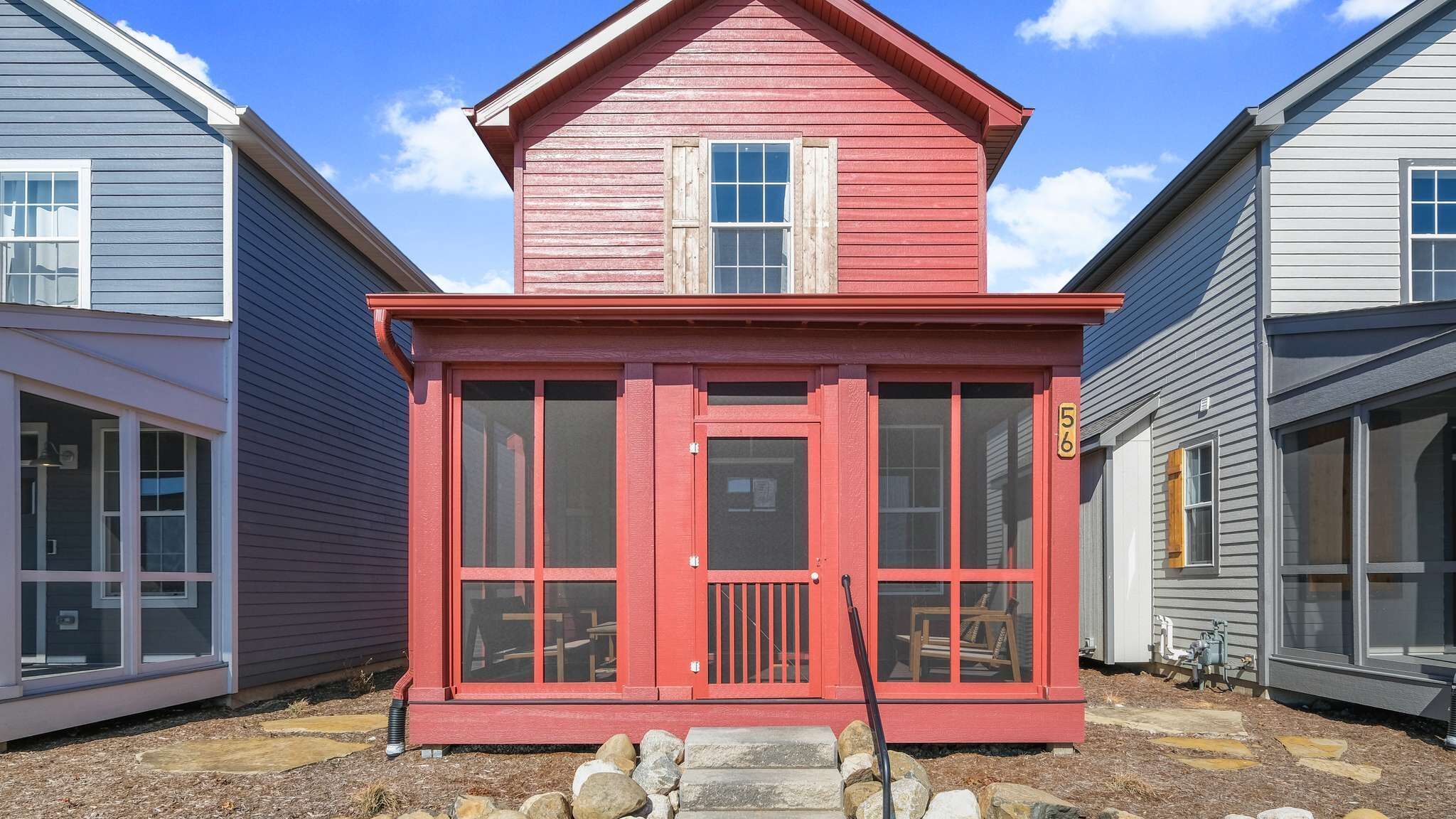 Une maison rouge à deux étages, avec un porche à l’avant, une petite fenêtre et une boîte aux lettres.