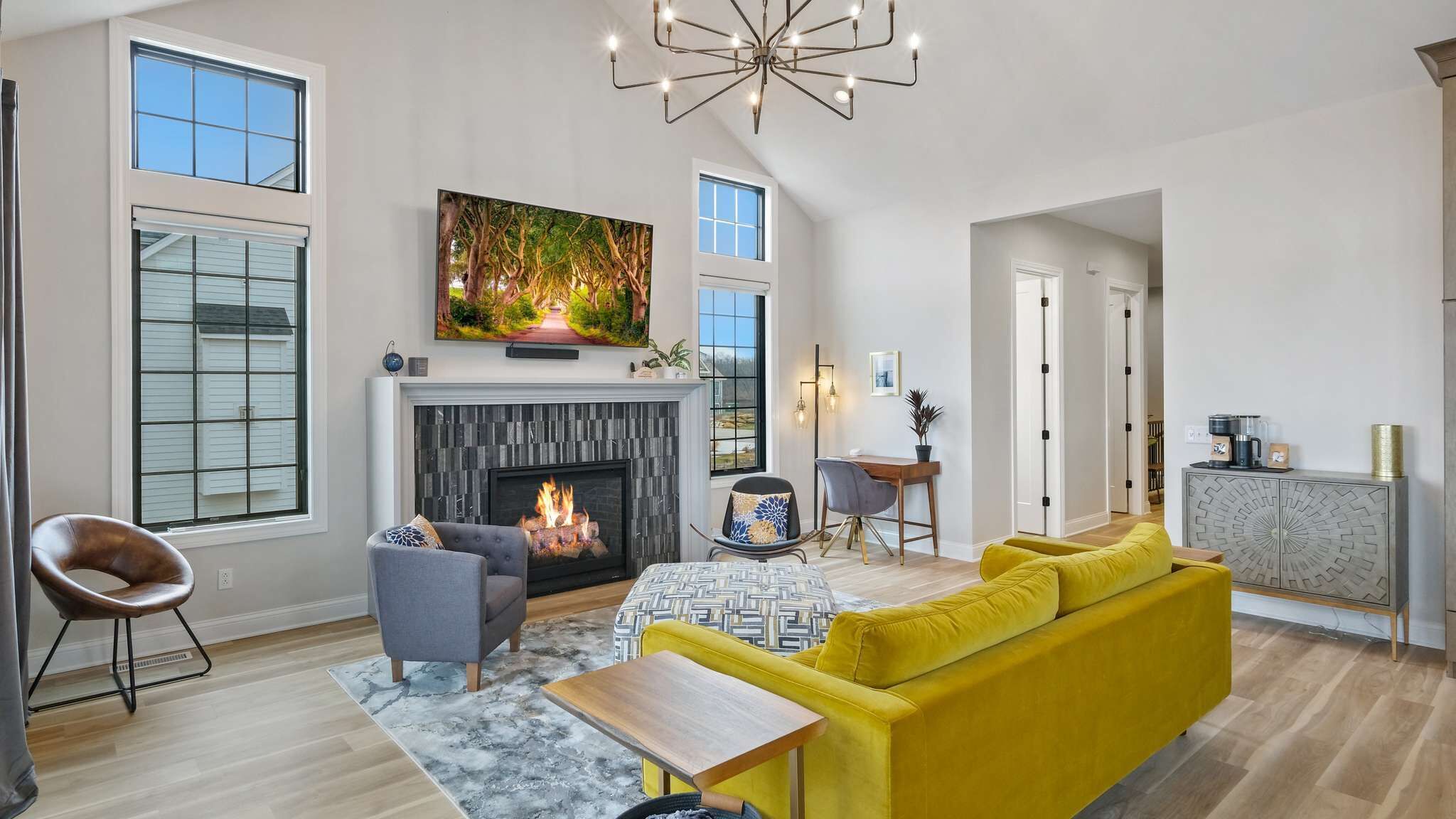 A spacious living room with a fireplace, a yellow sofa, a dining table, and a large TV mounted above the fireplace.