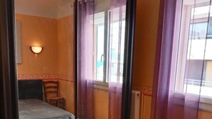 Ein Schlafzimmer mit Bett, Sessel, Wandleuchte und einem fensterbepflanzten Fenster.