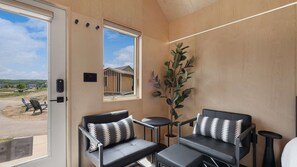 Un interior moderno con dos sofás de cuero negro, una mesita redonda y un amplio ventanal con vistas a un edificio y un estacionamiento.
