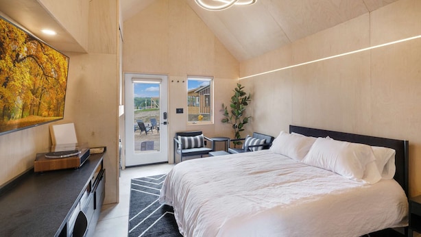 Une chambre moderne avec un grand lit, un bureau avec un ordinateur et une vue sur un espace extérieur grâce à une porte vitrée.