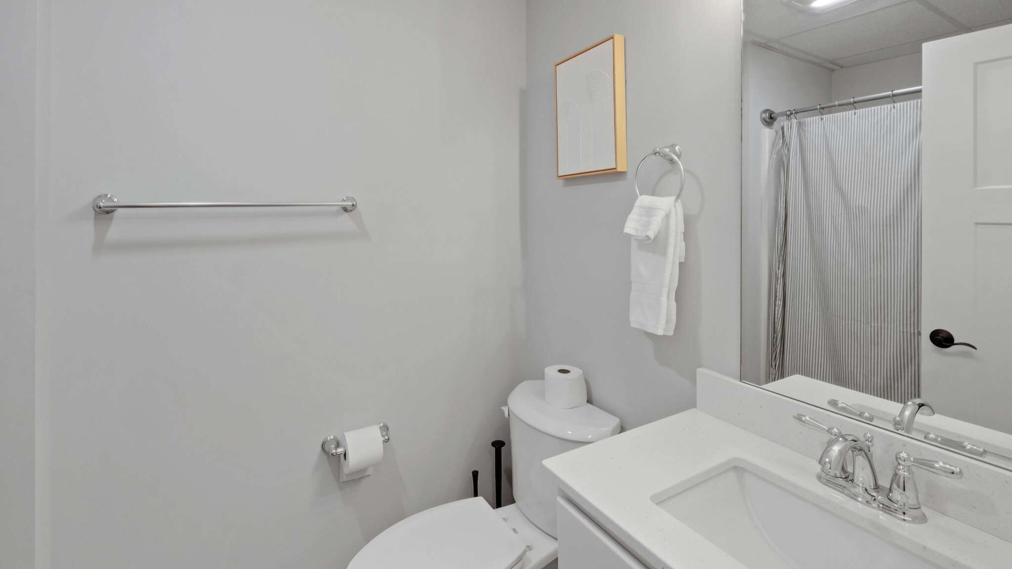 Ein Badezimmer mit Toilette, Waschbecken, Spiegel, Handtuchhalter und Duschvorhang.