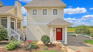 A two-story house with a red door, a covered porch, and a small garden with flowers and shrubs. - 2 Great Loop West - River Resort Cottage Community in Starved Rock Country (Ottawa)