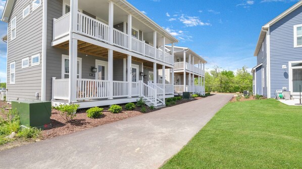 A two-story residential building with a covered porch, a driveway, and a well-maintained lawn.
