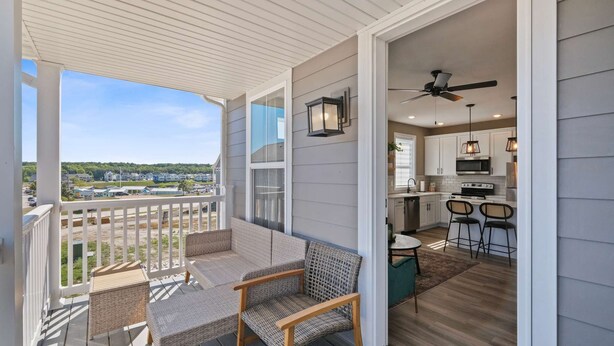 A covered balcony with wicker furniture, a kitchen with white cabinets, and a view of a residential area. - Dog Friendly Condo | Navvy Town Neighborhood (Ottawa)