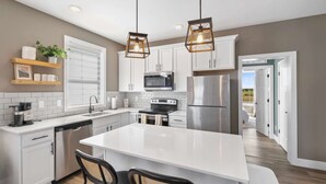 A modern kitchen with white cabinets, stainless steel appliances, and a central island with seating. - Dog Friendly Condo | Navvy Town Neighborhood (Ottawa)