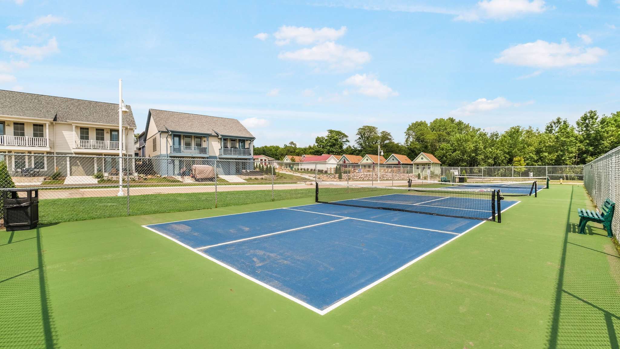 Tenniskenttä, jossa on verkko, ja kentän ympärillä on aita. Taustalla näkyy taloja.