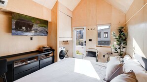 A bedroom with a bed, a TV mounted on the wall, a washing machine, a chair, and a window. - The Bunkies @ Heritage Harbor (Ottawa)