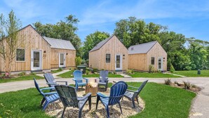 A row of wooden cabins with numbered doors, a fire pit, and outdoor seating. - The Bunkies @ Heritage Harbor (Ottawa)