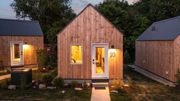 A small wooden cabin with a door and window, surrounded by a garden. - The Bunkies @ Heritage Harbor (Ottawa)