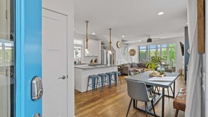 Uma cozinha moderna com uma ilha central, banquetas de bar, uma mesa de jantar com cadeiras e uma sala de estar com sofá e televisão.
