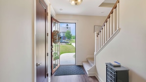 A hallway with a door leading to a backyard, a staircase, and a small cabinet.